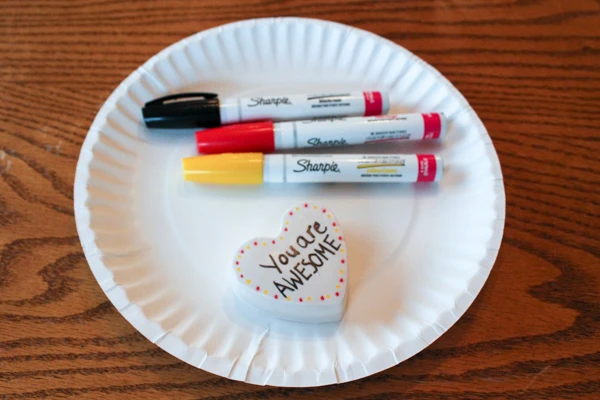 Decorate heart-shaped kindness rocks with oil-paint markers.